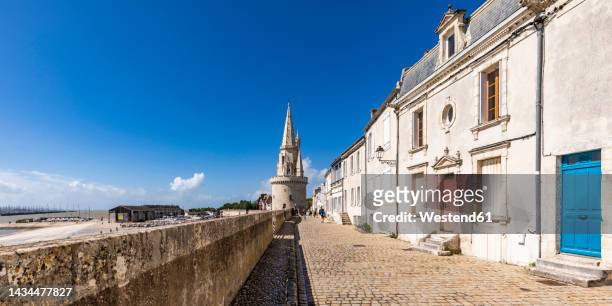 france, nouvelle-aquitaine, la rochelle, paved footpath with lantern tower in background - charente maritime stock pictures, royalty-free photos & images