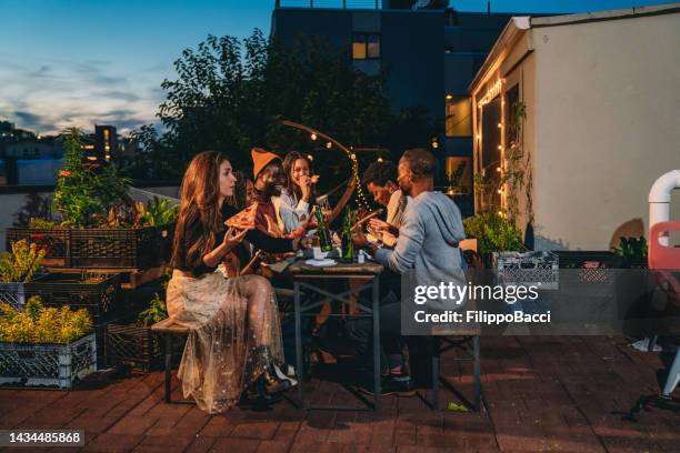 dinner party with friends on a rooftop at night - reünie sociaal stockfoto's en -beelden