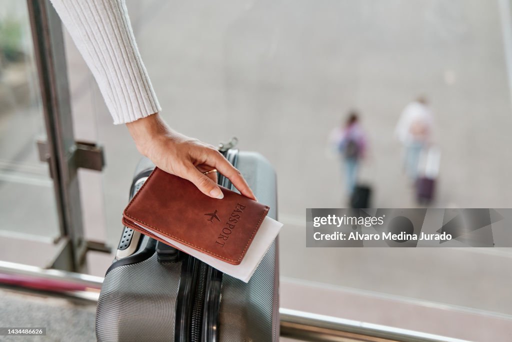 Woman hand with suitcase and passport waiting at airport terminal.