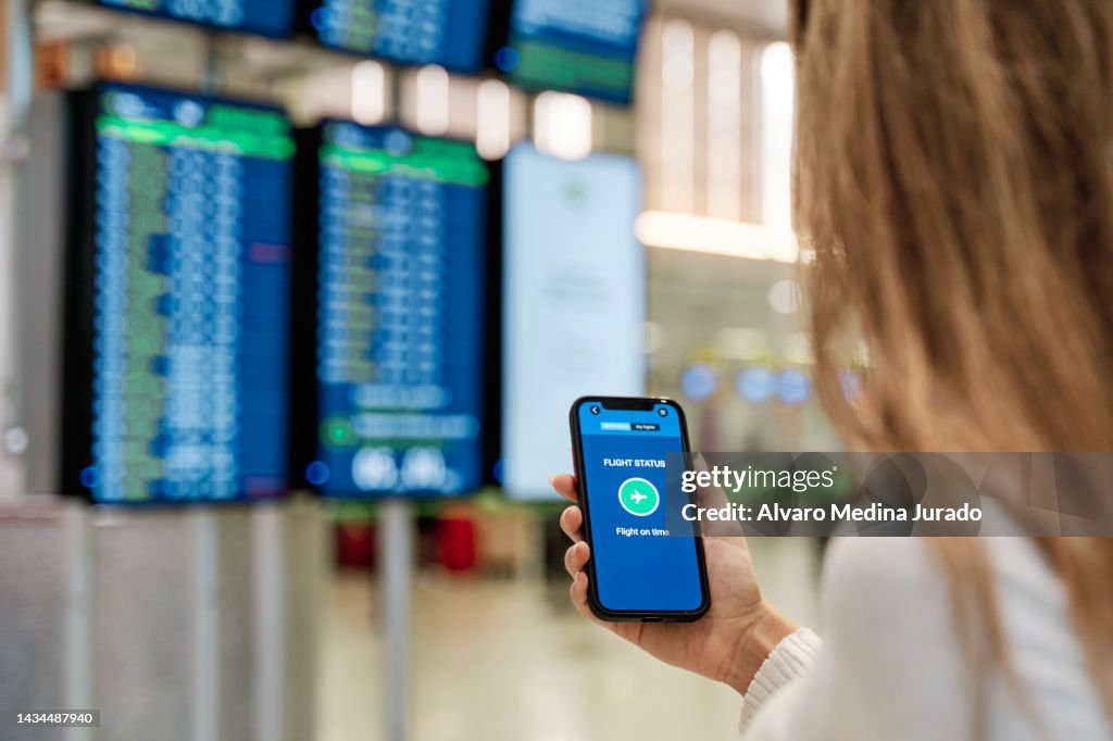 Close-up view of an unrecognizable woman's hand in airport terminal holding her mobile phone receiving a notification with her flight on time.