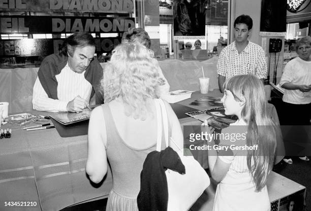 American Pop musician Neil Diamond signs an autograph for an unidentified woman, while a young girl waits beside her, during an in-store at Tower...