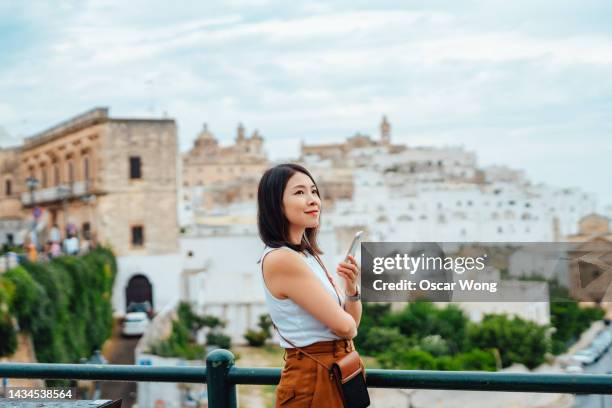 young asian woman using smart phone while overlooking the old town in ostuni, puglia, italy. - europe travel stock-fotos und bilder