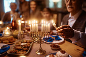 Close up of senior man lighting menorah during family dinner on Hanukkah.