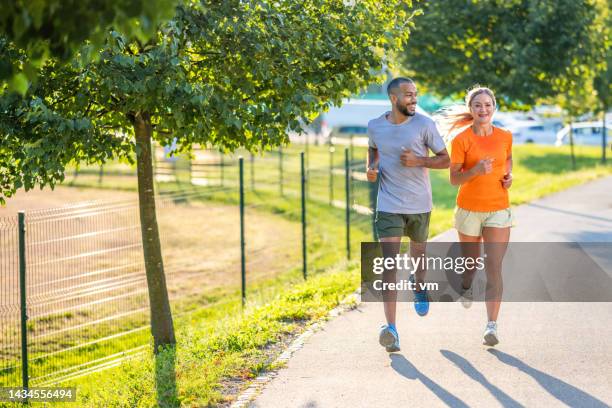 pareja joven sonriente trotando, charlando en el parque de la ciudad - carrera de carretera fotografías e imágenes de stock