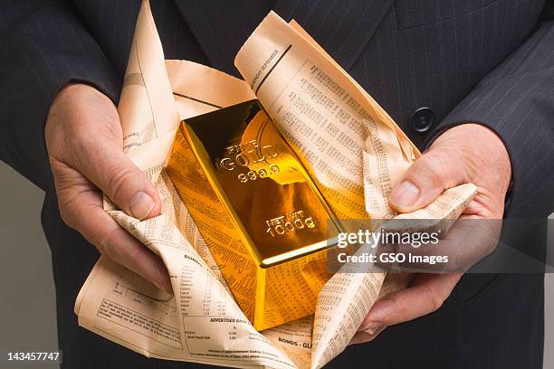 gold bar wrapped in a financial newspaper - gold bars stock pictures, royalty-free photos & images