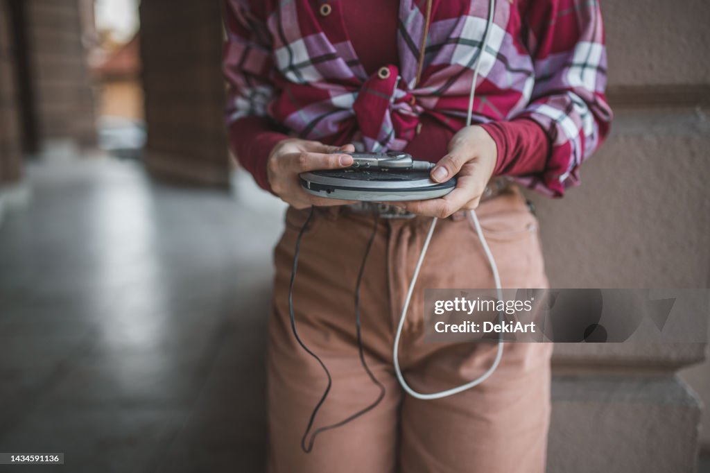 An unrecognizable woman listens to music with a disc player while walking around the city