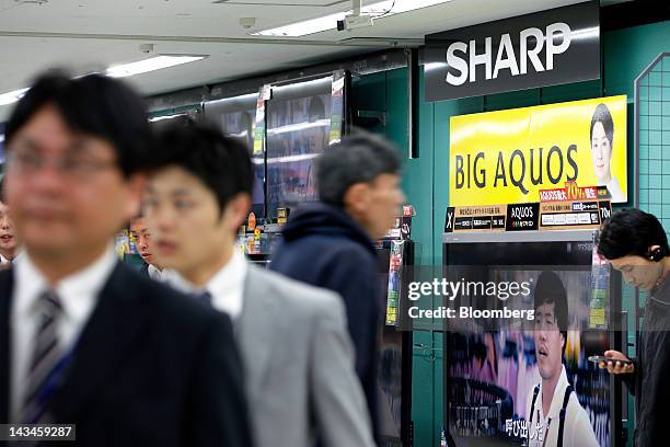 Customers walk past Sharp Corp. Aquos liquid crystal display televisions at the Labi Ofuna electronics store, operated by Yamada Denki Co., in...