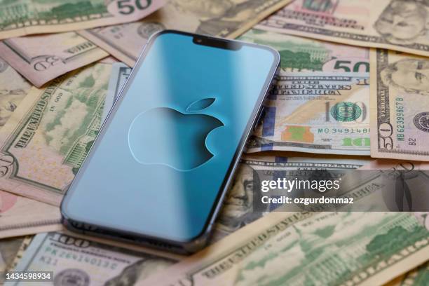 apple iphone 13 pro smartphone with apple logo on the screen stands over us dollar banknotes - big tech money stock pictures, royalty-free photos & images