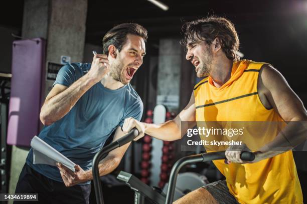 happy coach cheering for athletic man on stationary bike in a gym. - spin instructor stock pictures, royalty-free photos & images