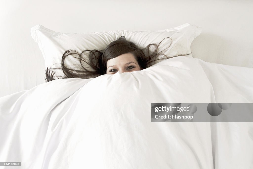 Woman in bed peering over top of duvet