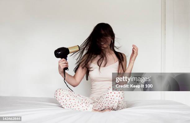 woman sitting on bed blow drying hair - secador de pelo fotografías e imágenes de stock