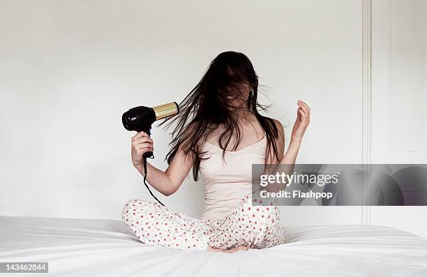 woman sitting on bed blow drying hair - hair dryer foto e immagini stock