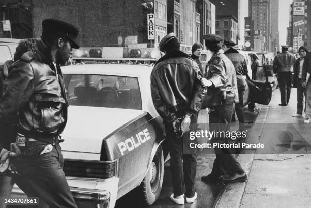 New York City Police Department officers on a street with a handcuffed arrestee standing beside an NYPD police car, in Midtown Manhattan, New York...