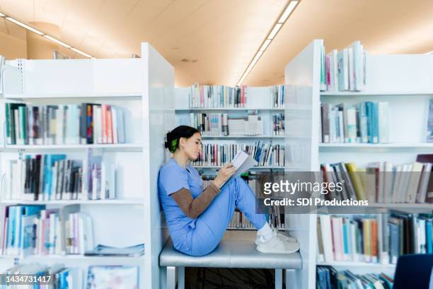 female intern finds quiet spot in library to study - doctor reading stock pictures, royalty-free photos & images