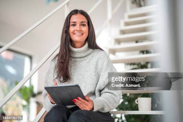 portrait of a smiling young caucasian female holding a digital tablet on a cozy autumn morning at home - digitalization stock pictures, royalty-free photos & images