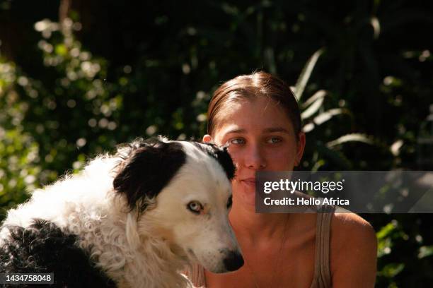 a beautiful young woman sitting in the sunlight with a black & white border collie, a teenage girls with long brown hair worn back in a middle parting looks away from camera whilst sitting with a dog in front of her that looks at camera - border collie foto e immagini stock