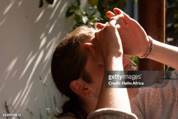 a young man shades his eyes that are concealed from view, a teenage boy with long brown hair worn tied back & wearing a loop earring makes a peak with his hands as he looks up towards the sky & sun - hands sun stock-fotos und bilder