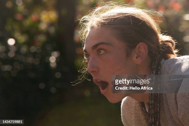profile view of a handsome young man looking away from camera with mouth open wide, a teenage boy with long brown hair worn tied back looks way at something or someone with a look of surprise or wonder on his face - face and profile and mouth open stock-fotos und bilder