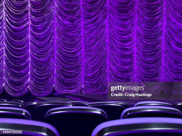 darkly lit luxury purple theatre curtain with a view of a few rows of seats. arts, theatre, show business, entertainment and cinema concept - musical theater stock-fotos und bilder