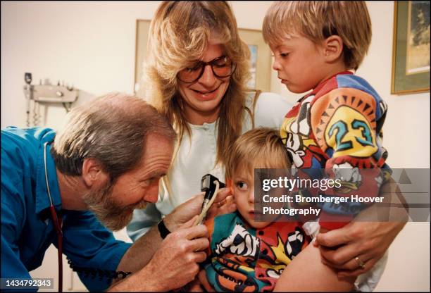 View of a family doctor examining a young boy's ear, as the boy's mother and brother watch, Okanogan, Washington, 1994.