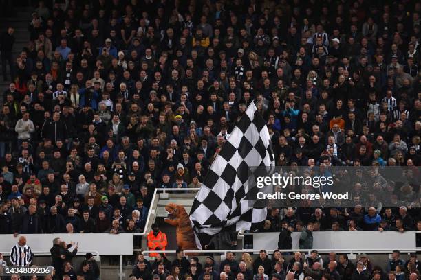 Newcastle United fan, wearing an inflatable T-Rex costume, waves a large White and Black chequered flag during the Premier League match between...