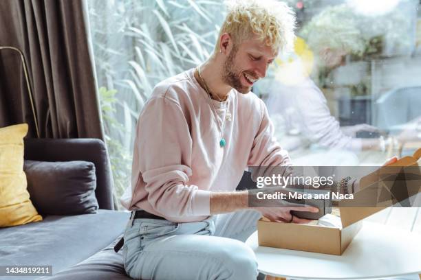 happy young blond man looking at a product he bought online - beautiful gay men stock pictures, royalty-free photos & images