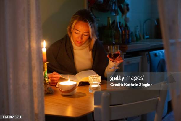 woman reading a book illuminated by candlelight, avoiding to use electricity - no electricity stock pictures, royalty-free photos & images