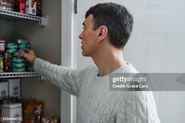 man searches kitchen pantry for food - speisekammer stock-fotos und bilder