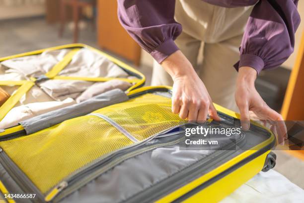 female hands packing luggage, closing zipper in open yellow suitcase, close up - bezittingen stockfoto's en -beelden