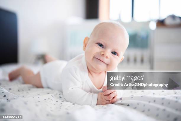 pequeño bebé alegre acostado al frente en la cama. - un solo niño bebé fotografías e imágenes de stock