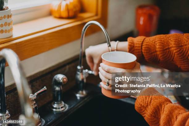 filling a mug with water from faucet - purified water stock-fotos und bilder