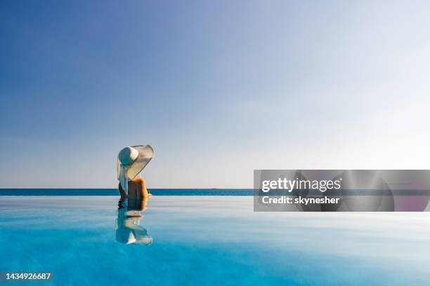 woman with sun hat looking at view from an infinity pool. - infinity pool stockfoto's en -beelden