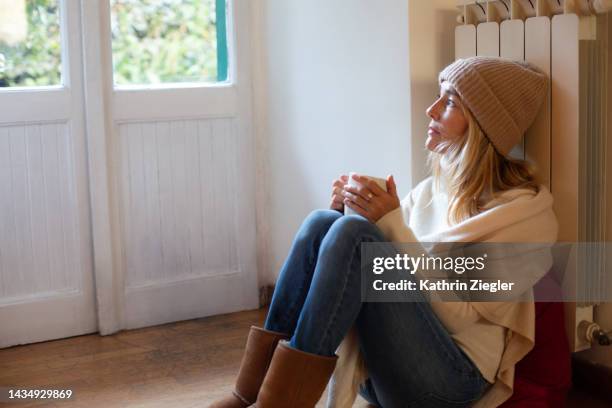 woman leaning against the heating in warm clothing - heating home stock pictures, royalty-free photos & images