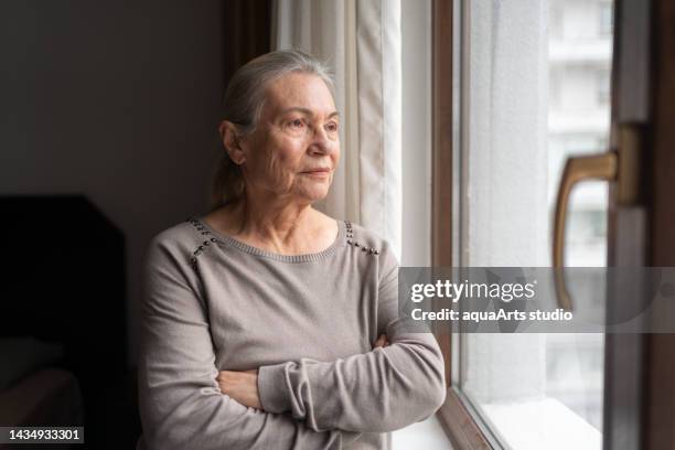 lonely senior woman looking through the window - introspection stock pictures, royalty-free photos & images