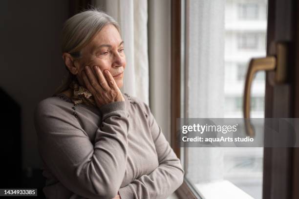 lonely senior woman looking through the window - daydreaming sad stock pictures, royalty-free photos & images