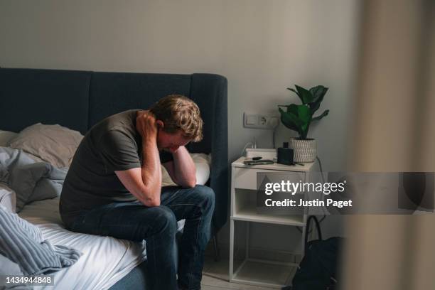 mature male sitting on his bed - negative emotion - depresión fotografías e imágenes de stock