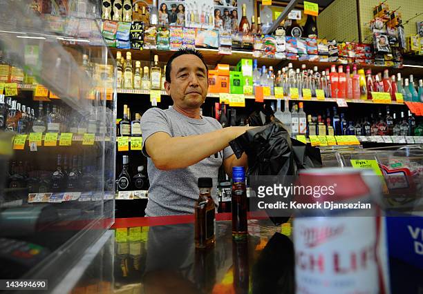 James Oh, owner of Tom Liquor store located at the intersection of Florence and Normandy Avenues in South Los Angeles, waits on a customer on April...