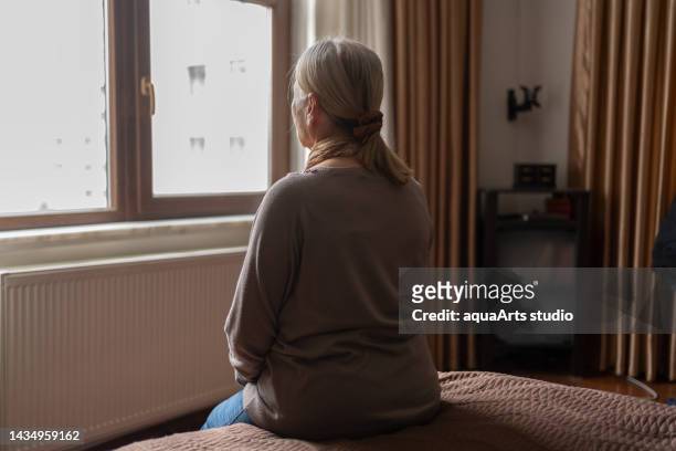 senior woman looking out the window - eenzaamheid stockfoto's en -beelden