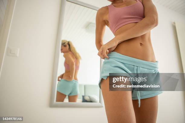 young woman checking herself in the mirror - slank stockfoto's en -beelden