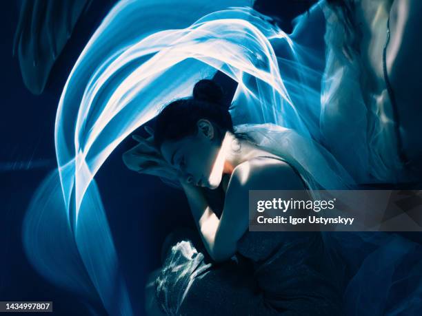 young dreamy woman with flashes of white and blue light - position du foetus photos et images de collection