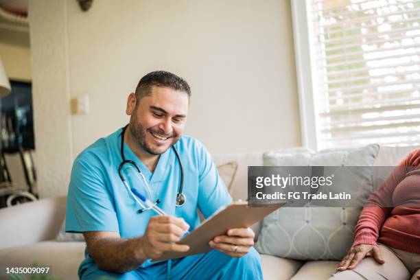 krankenschwester im mittleren erwachsenenalter, die mit einem klienten in einer konsultation im wohnzimmer eines pflegeheims spricht - client carer stock-fotos und bilder