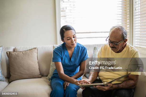 senior man and nurse looking at photo album in the living room in a nursing home - assisted living community stock pictures, royalty-free photos & images