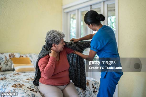 krankenschwester für mittlere erwachsene, die älteren frauen hilft, hemd im schlafzimmer des pflegeheims zu kleiden - anziehen stock-fotos und bilder