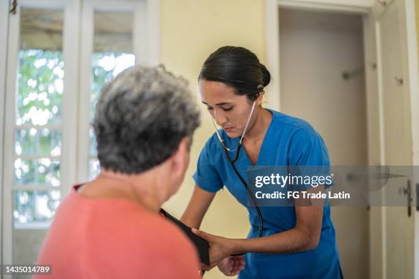 infirmière mi-adulte mesurant la pression d’une femme âgée dans la chambre à coucher d’une maison de soins infirmiers - infirmière et maison photos et images de collection