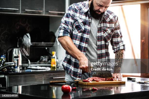 middle aged man with beard cutting fresh beef meat in the kitchen - red meat stock pictures, royalty-free photos & images