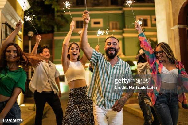 friends walking while playing with sparklers on the street at night - street party stock pictures, royalty-free photos & images