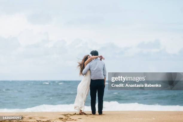 groom and bride hugging and looking toward the ocean. beach wedding, kauai, hawaii - newlywed stock pictures, royalty-free photos & images