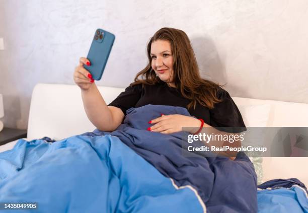 woman taking a selfie in bed wearing pajamas - nightdress stock pictures, royalty-free photos & images