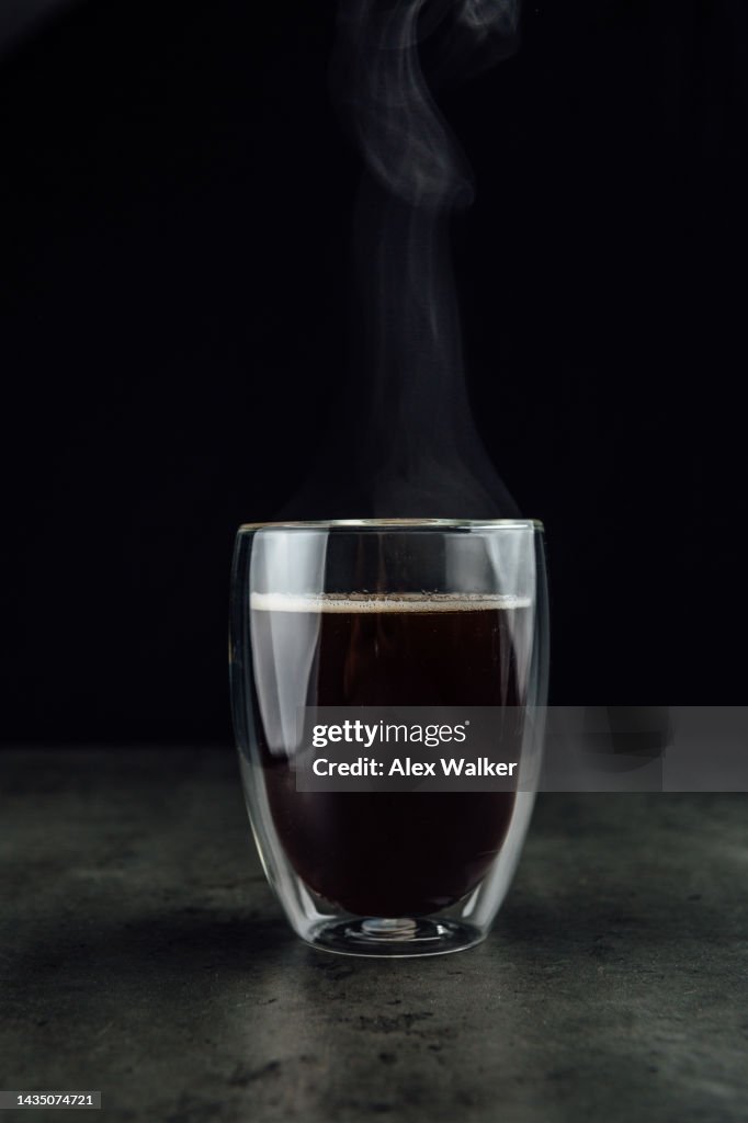 Mug of black coffee in a modern glass coffee mug on a textured table.