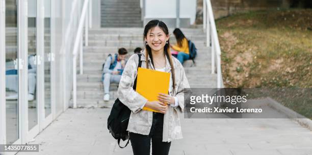 smiling cheerful young adult asian female student standing outdoors at university campus smiling at camera - education and college concept - chinese female university student portrait fotografías e imágenes de stock